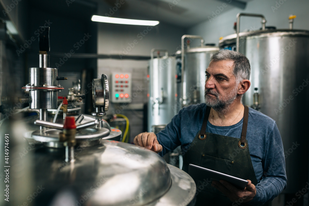brewer working on digital tablet in his craft beer brewery. He is examining the process of making beer brewer working on digital tablet in his craft beer brewery. He is examining the process of making beer