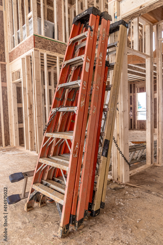 Fototapeta premium Red, orange, yellow tall aluminum construction ladders leaning on each other in the living room of a luxury house under construction in the USA 
