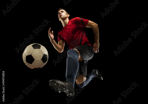 Young caucasian football, soccer player in action, motion isolated on black background, look from the bottom. Concept of sport, movement, energy and dynamic, healthy lifestyle. Training, practicing.
