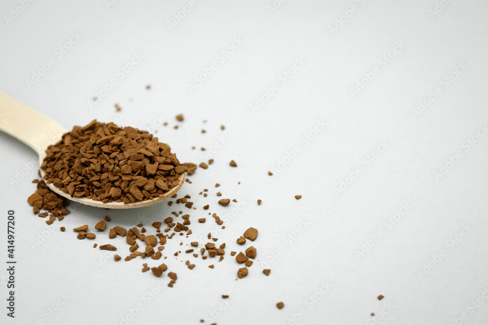 A wooden spoon with instant coffee on the table. Light background. Coffee scattered around. No waste concept. Space for the text on the right. A wooden spoon with instant coffee on the table. Light background. Coffee scattered around. No waste concept. Space for the text on the right.