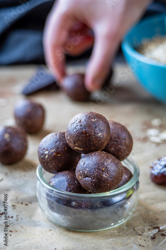 Healthy energy protein balls with dates, oats, peanut butter and dark chocolate. Homemade gluten free truffle bites with no bake. Vegan and vegetarian raw appetizer or food snack. Hand in background