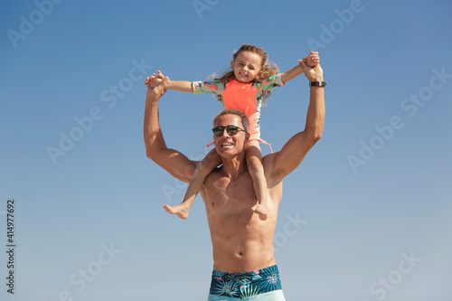 Un padre prende la figlia sulle spalle giocando simpaticamente con lei al mare in spiaggia photo