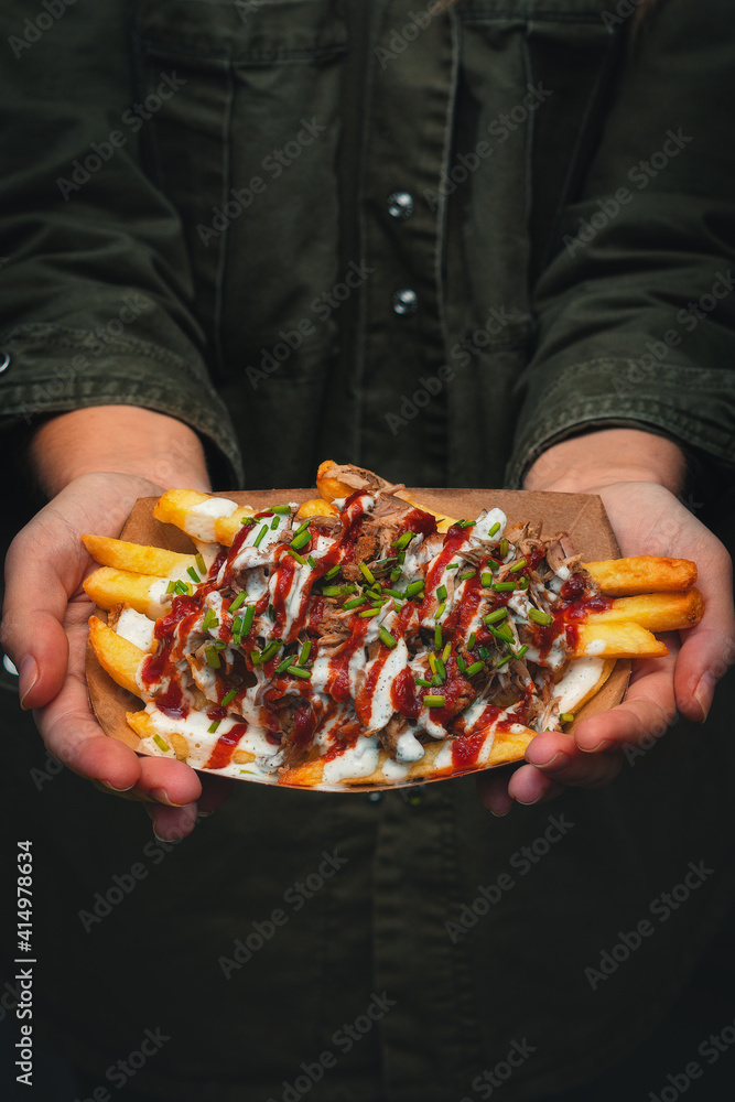 Close view of the hands of a young girl holding a portion gourmet french fries with white and red sauces (mayonnaise and ketchup)