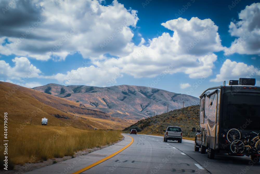 Obraz premium Driving through dry bare mountains on divided highway behind a camper and other vehicles