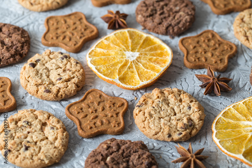 Oatmeal, ginger and chocolate cookies, slices of dried oranges, stars of anise on a textured gray background