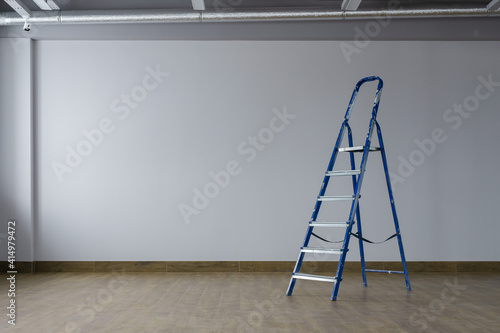 A dirty blue metal stepladder against of drywall gray painted  in a new building. The concept of professional renovation. Copy space.