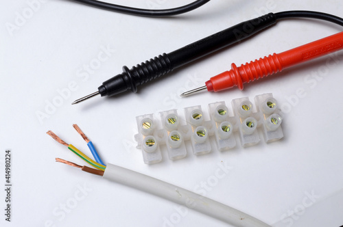 stripped three-core wire, terminal block and multimeter probes. light background. close-up.