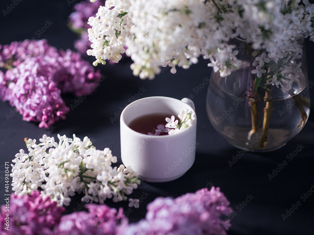 a cup of tea and flowering branches of white and purple lilac on a dark background a cup of tea and flowering branches of white and purple lilac on a dark background