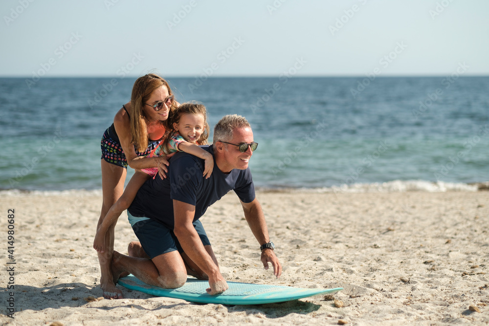 Obraz premium Allegra famiglia composta da padre, madre e figlia si diverte giocando con con una tavola da surf in spiaggia al mare