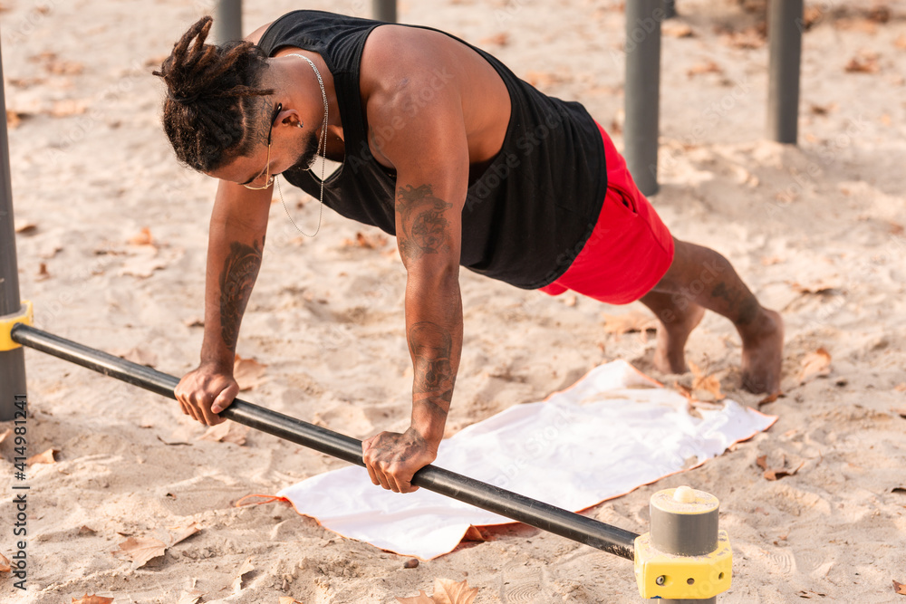 african american boy does push-up exercises on a barbell in a calisthenics park. african american boy does push-up exercises on a barbell in a calisthenics park.