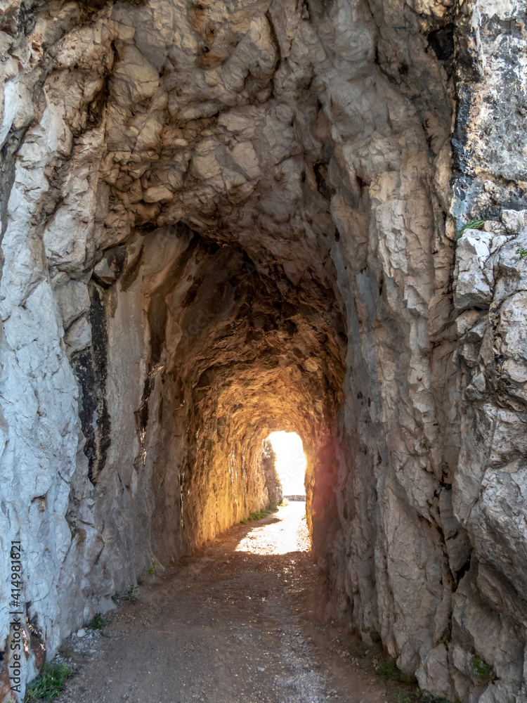 chemin de randonnée passant dans un tunnel creusé dans la roche et avec le soleil inondant la sortie
