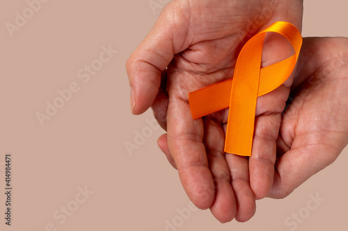 Hands holding orange ribbon to raise awareness about leukemia, kidney cancer, multiple sclerosis. Campaign in February or December. Space for text. photo