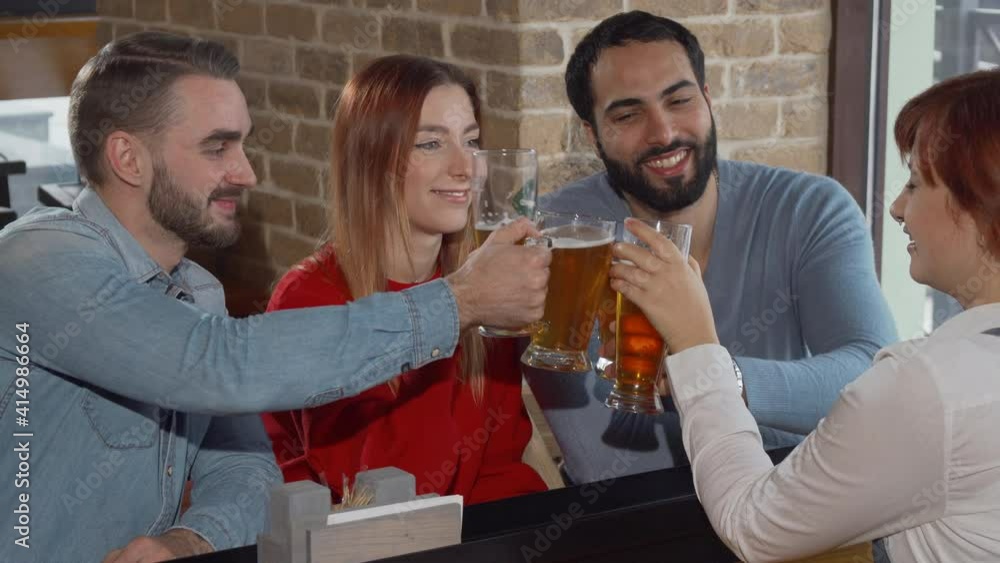 Happy friends toasting with their beer glasses at the pub. Group of young people celebrating together at the bar, drinking beer, clinking their glasses. Friendship, recreation concept Happy friends toasting with their beer glasses at the pub. Group of young people celebrating together at the bar, drinking beer, clinking their glasses. Friendship, recreation concept