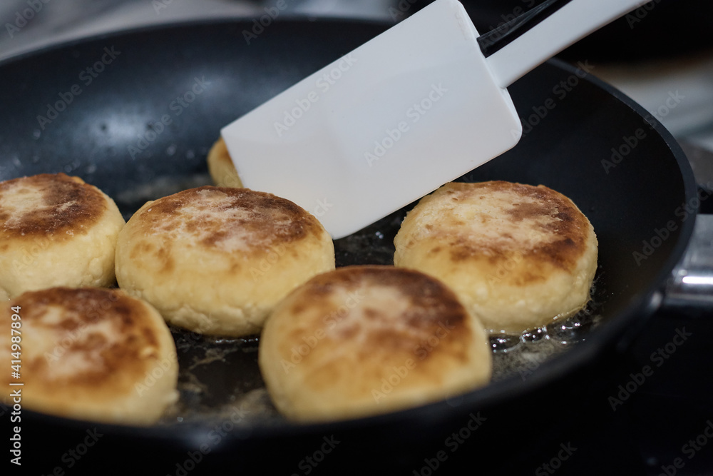 cheesecakes are fried in a frying pan the cook turns the dough with a spoon close up the background is blurred cheesecakes are fried in a frying pan the cook turns the dough with a spoon close up the background is blurred