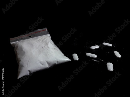Cocaine drug powder in bag and pills on black background