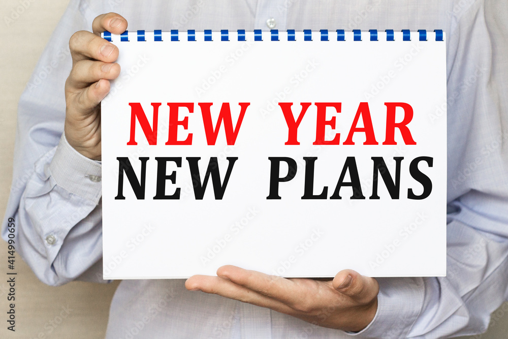 The businessman shows a sheet with the text NEW YEAR NEW PLANS on a white background. Business concept The businessman shows a sheet with the text NEW YEAR NEW PLANS on a white background. Business concept
