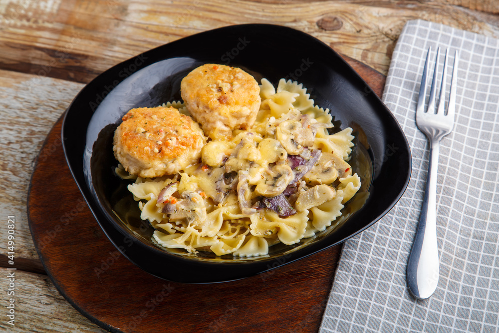 Pasta in a creamy sauce with mushrooms and chicken meatballs in a black plate on a napkin next to a fork. Pasta in a creamy sauce with mushrooms and chicken meatballs in a black plate on a napkin next to a fork.