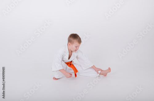 little boy in a white kimono with an orange belt does a warm-up on a white background with space for text photo