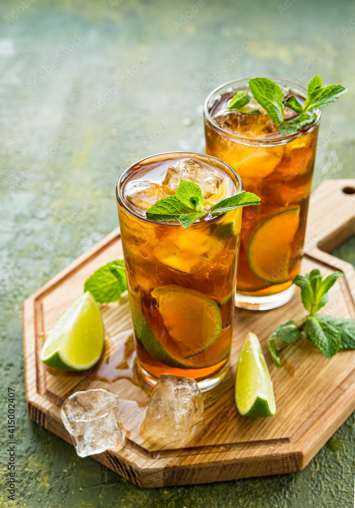 Refreshing drink, iced tea with lime wedges in glasses on a wooden board on a green concrete background. Summer drinks. Refreshing drink, iced tea with lime wedges in glasses on a wooden board on a green concrete background. Summer drinks.