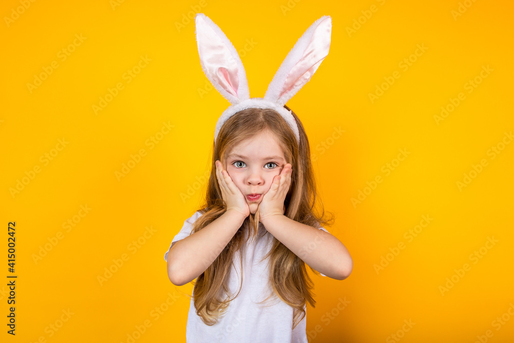 Portrait of a surprised Easter girl with bunny ears on a yellow background holding her face with her hands Portrait of a surprised Easter girl with bunny ears on a yellow background holding her face with her hands