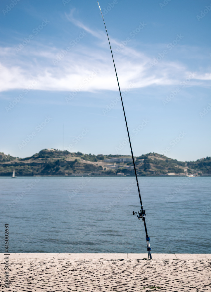A fishing rod standing along the Lisbon riverbank of Tagus river near the Belem tower at sunset. Fisherman lifestyle