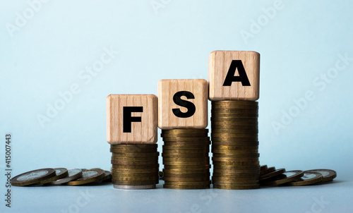 FSA - acronym on wooden cubes. Which stand on stacks of coins on a light background