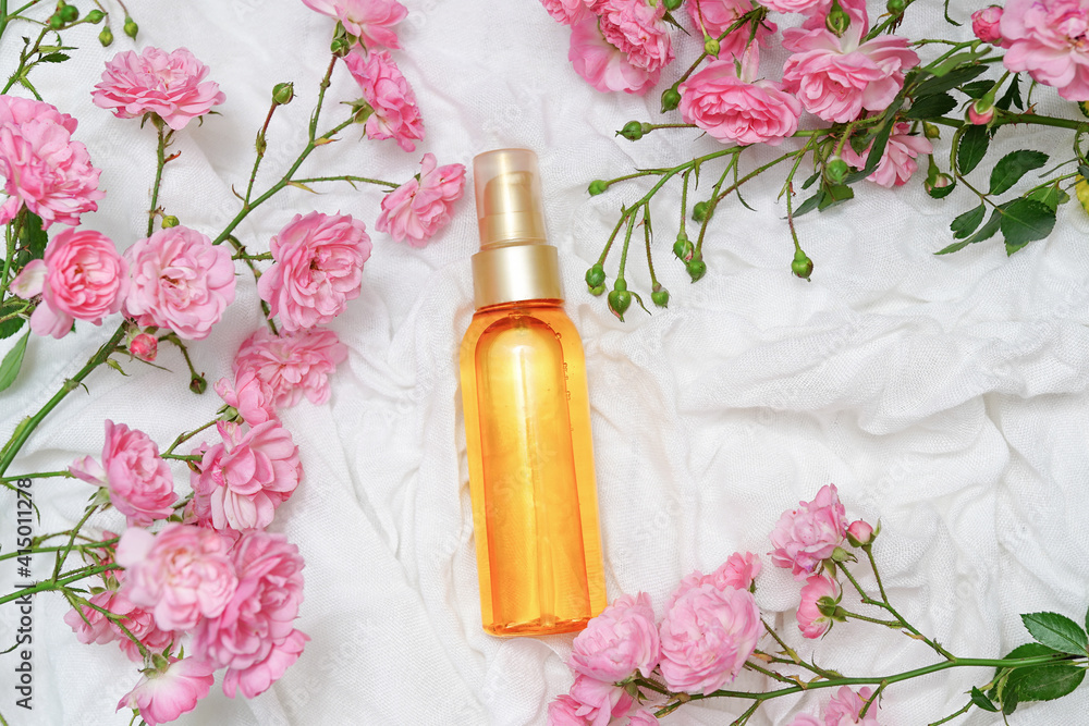 Bottle of essential aromatic oil and fresh flowers pink roses on white Bottle of essential aromatic oil and fresh flowers pink roses on white