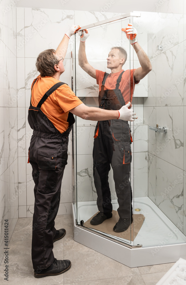 Workers are installing glass door of the shower enclosure. Stock Photo