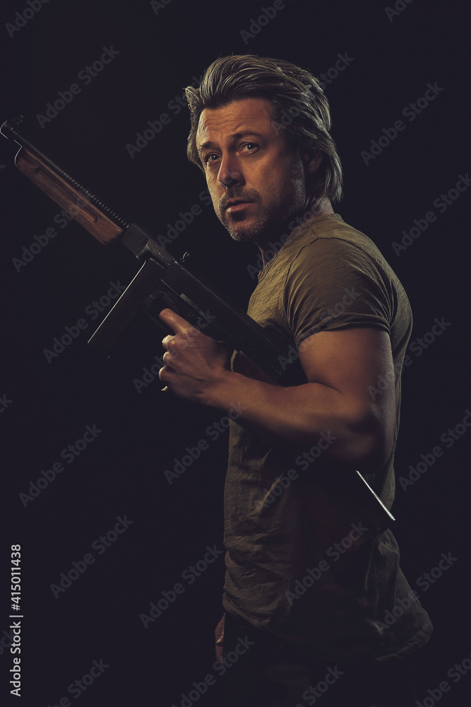 Rugged man with gun in green t-shirt against dark background. Rugged man with gun in green t-shirt against dark background.