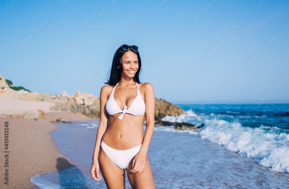 Happy slim girl 30 years old standing at coastline looking away and laughing during sunbathing weekend at beach, joyful female swimmer enjoying summer vacations for recreating nature environment