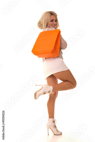 Beautiful girl posing at the camera with a package in her hands. Girl lifted her leg and holds the purchase after black friday.