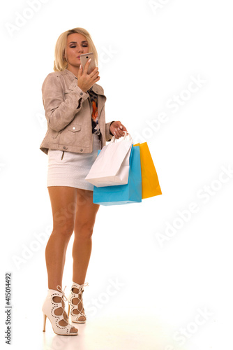 Girl looks at a mobile phone while standing with purchases after Black Friday. Blonde with a phone and packages in her hands after a day of discounts.