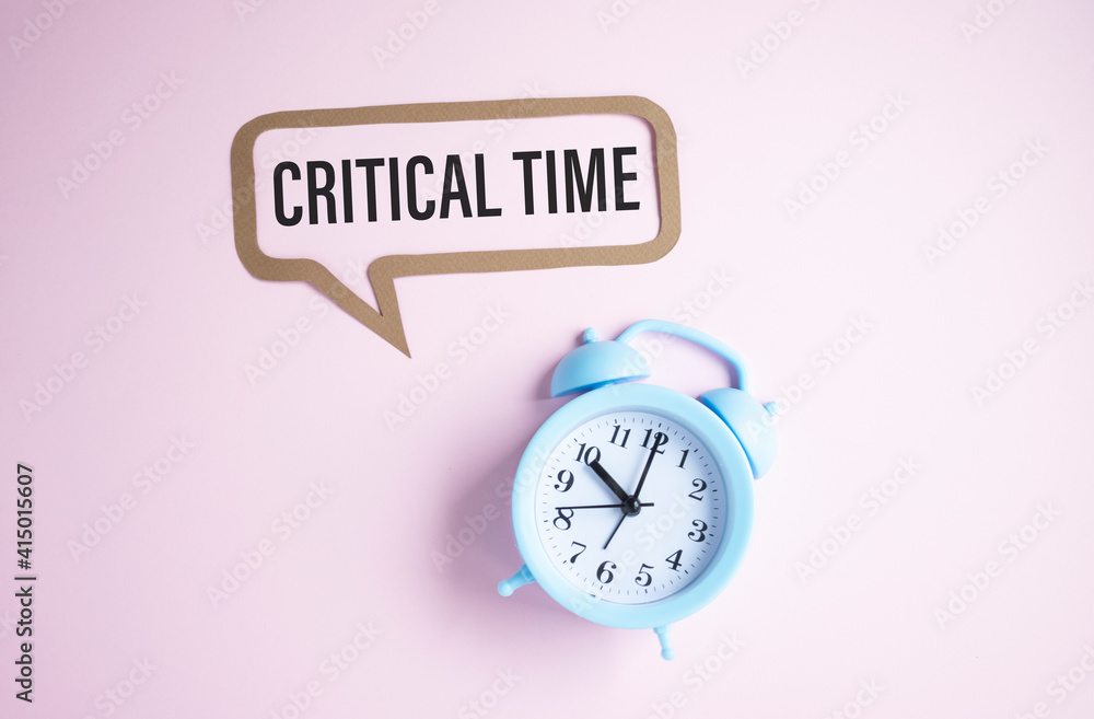Critical time - text on light pink background with blue alarm clock ...