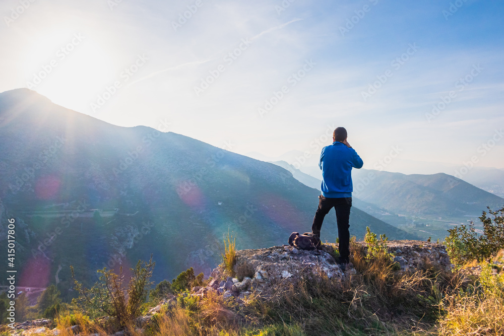 Fototapeta premium Photographer taking photos from the top of a mountain, to a natural landscape, with the sun and mountains in the background.