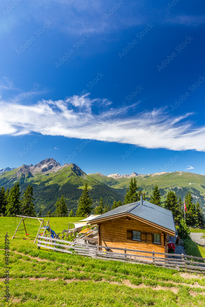 Alpine hut with Swiss flag, beneath stunning clouds. Surses, Surselva, Graubunden, Switzerland Alpine hut with Swiss flag, beneath stunning clouds. Surses, Surselva, Graubunden, Switzerland