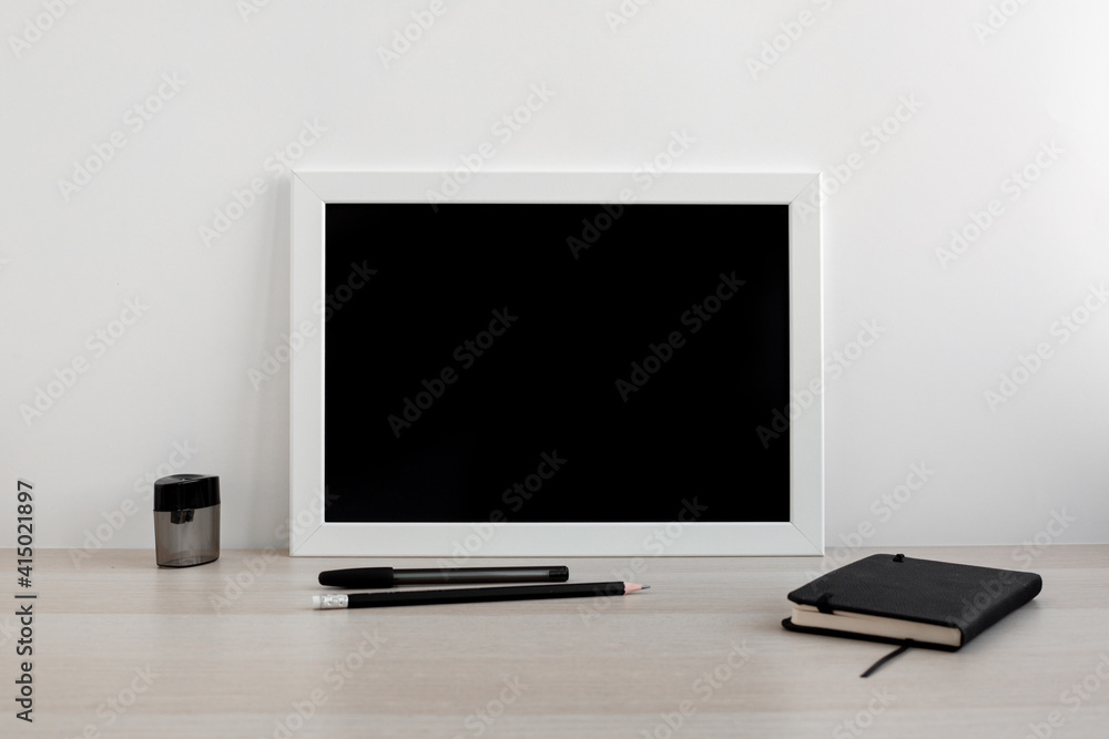 White frame with black background in a bright room on the desktop. Notebook and pens in the workplace. Minimalistic design White frame with black background in a bright room on the desktop. Notebook and pens in the workplace. Minimalistic design