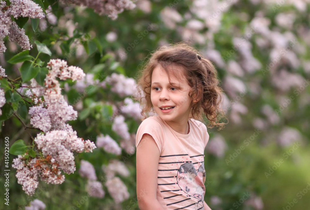 Portrit of happy smiling little girl on blooming syringa bush background in spring park.