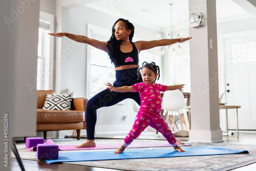 Black Mother and daughter doing yoga in family room, warrior pose