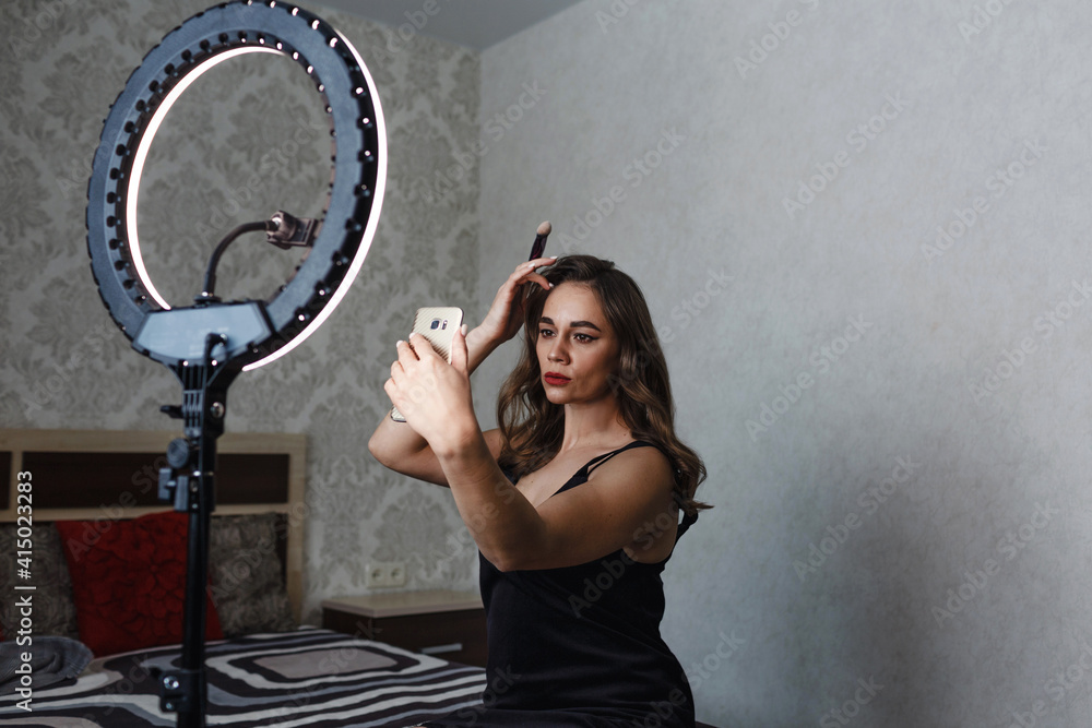 Fototapeta premium the girl puts makeup on her face and takes pictures of herself on the phone.