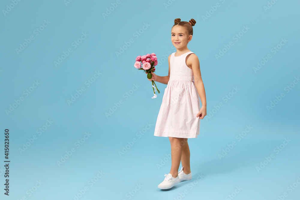 smiling little girl holds bouquet of roses on blue studio background. Mother's day. Copy space for text.