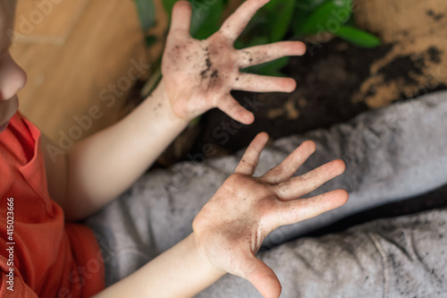  Child showing at dirty soil hands sitting on the floor with a broken pot of flowerpot. 