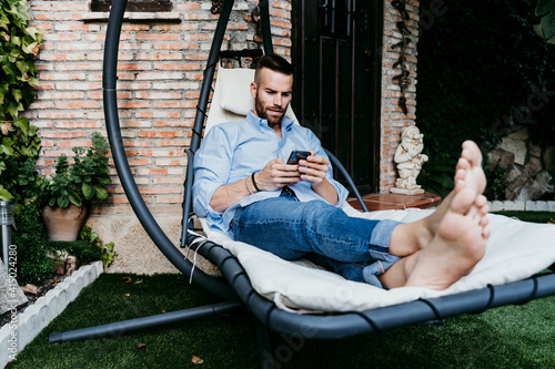 Young man working with mobile phone while sitting in hammock on terrace photo