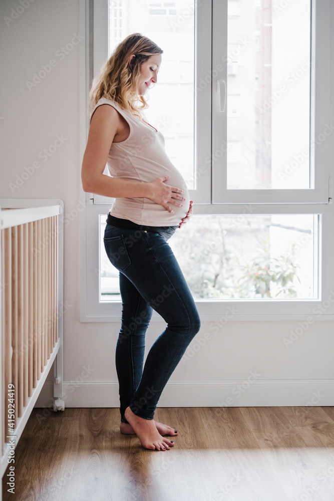 Pregnant mother with hands on stomach anticipating while standing by window Pregnant mother with hands on stomach anticipating while standing by window