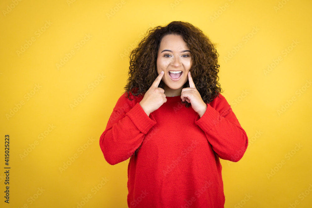 Young african american woman wearing red sweater over yellow background smiling confident showing and pointing with fingers teeth and mouth Young african american woman wearing red sweater over yellow background smiling confident showing and pointing with fingers teeth and mouth