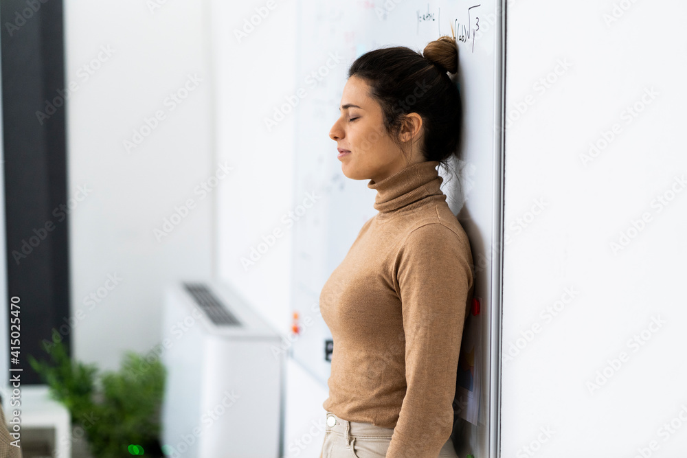 Tired female student with eyes closed leaning on whiteboard at home Tired female student with eyes closed leaning on whiteboard at home