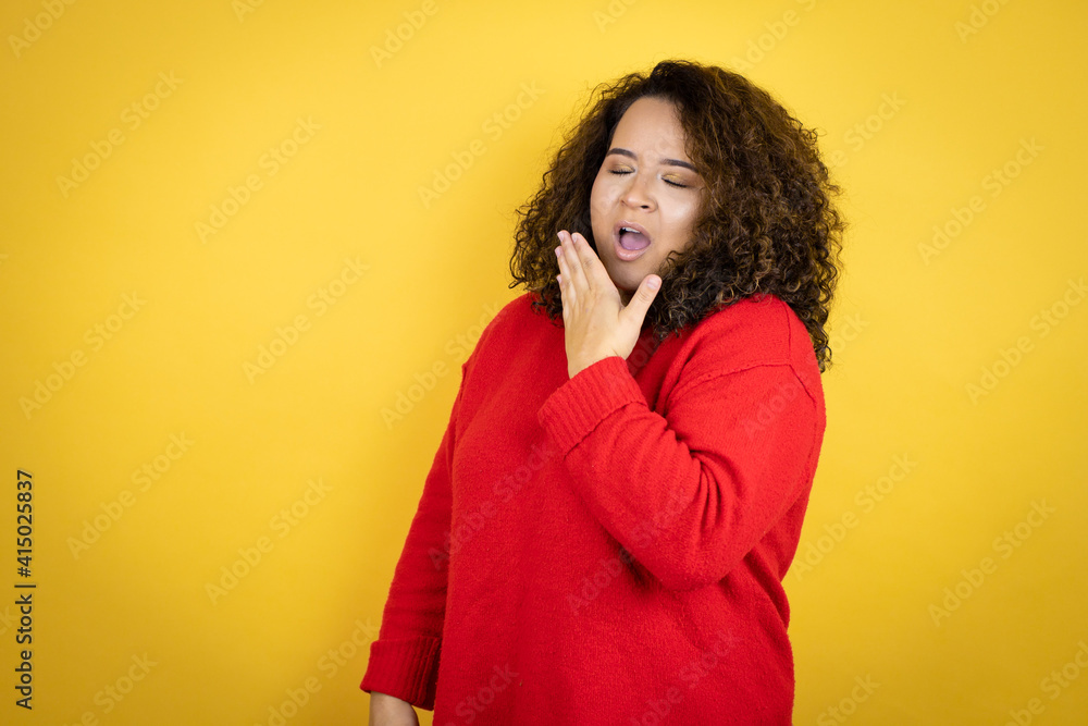 Young african american woman wearing red sweater over yellow background bored yawning tired covering mouth with hand. Restless and sleepiness. Young african american woman wearing red sweater over yellow background bored yawning tired covering mouth with hand. Restless and sleepiness.