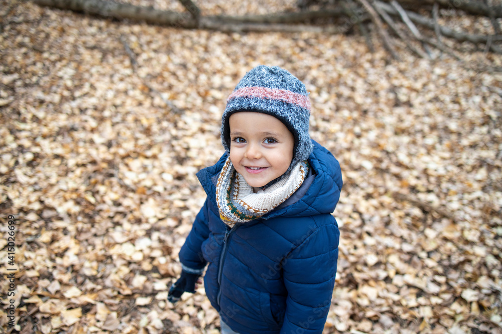 Cute boy wearing warm clothing standing on autumn leaves in forest Cute boy wearing warm clothing standing on autumn leaves in forest