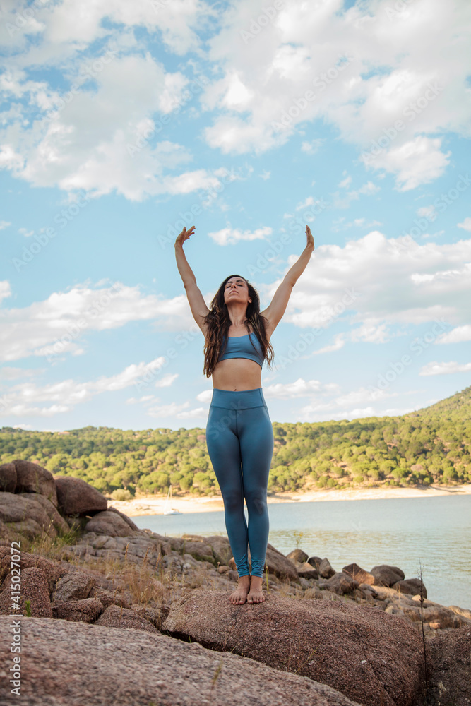 Woman practicing yoga with arms raised on rock against sky Woman practicing yoga with arms raised on rock against sky