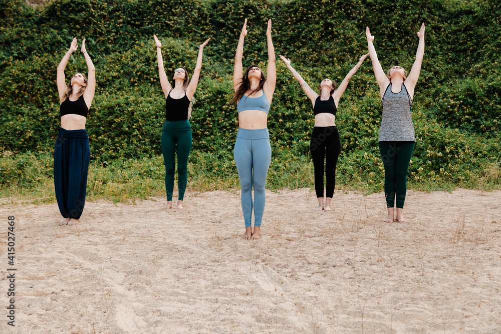 © Manu Reyes/Westend61 - Women and yoga instructor exercising with arms raised on sand against plants © Manu Reyes/Westend61 - Women and yoga instructor exercising with arms raised on sand against plants