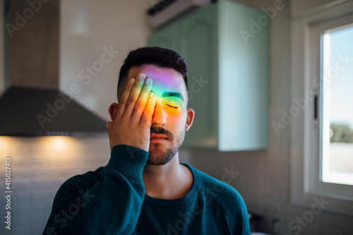 Rainbow light hitting face of¬†young man covering one eye with hand photo